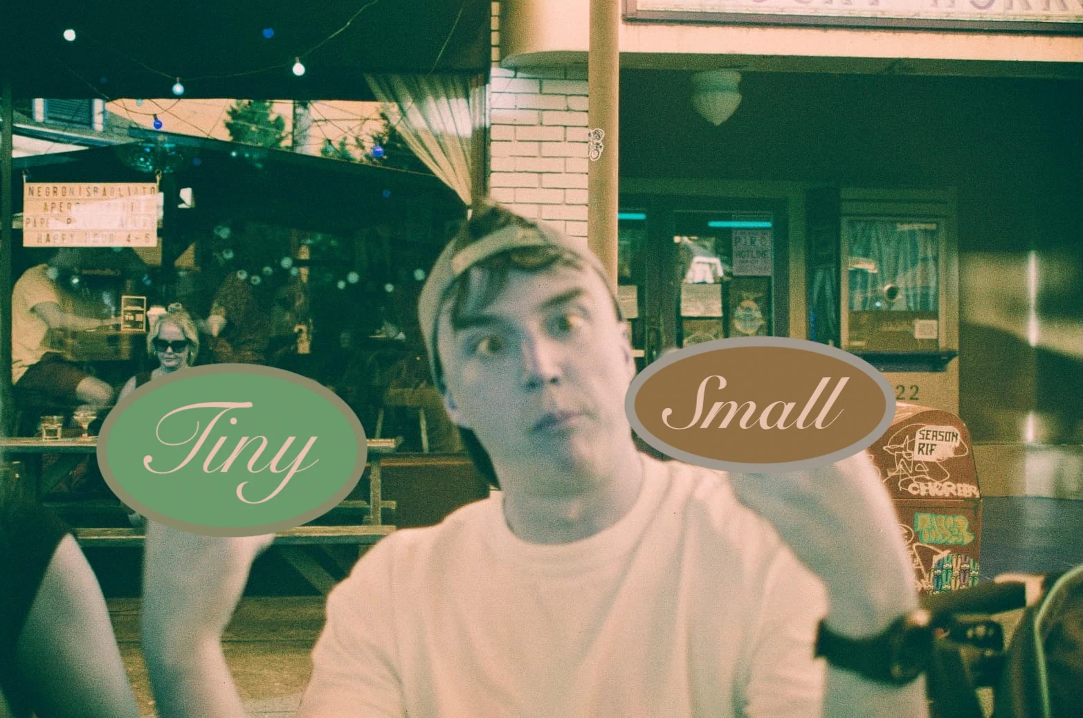 Tiny Small Productions — grainy night photo of a man with a surprised expression at an outdoor bar, with the brand name written in three decorative ovals reading Tiny, Small, and Productions.